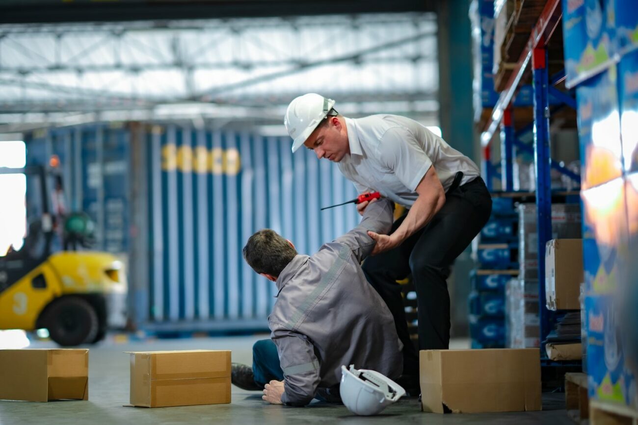 young worker rushes to help injured senior colleague who fell in warehouse team support, safety response, and workplace accident awareness